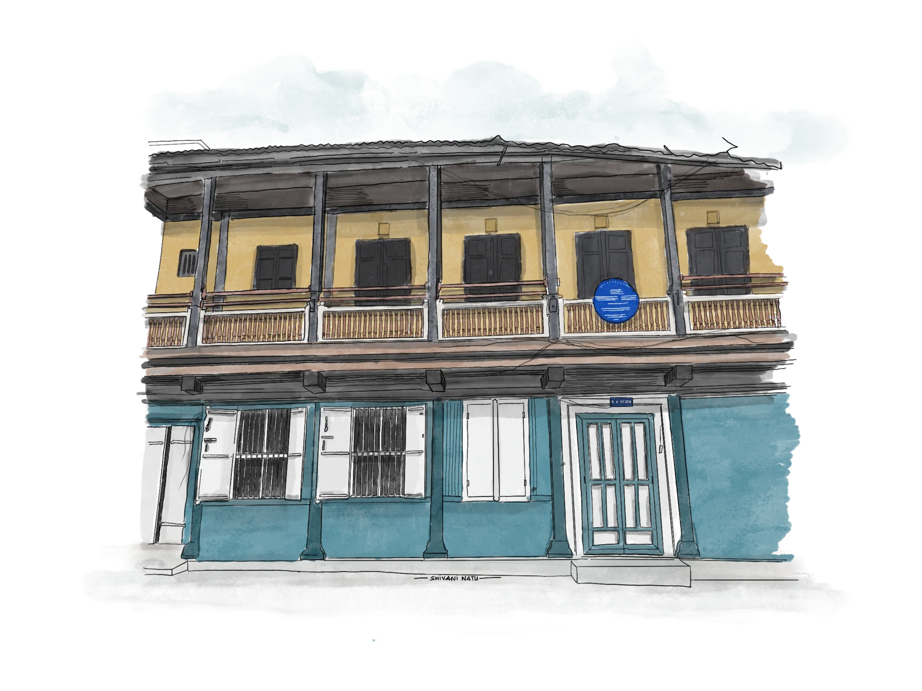 Two-storey heritage wada facade, mustard-yellow upper floor with dark shutters and turned-wood balcony rail over a teal ground floor with white shuttered windows and a blue heritage plaque